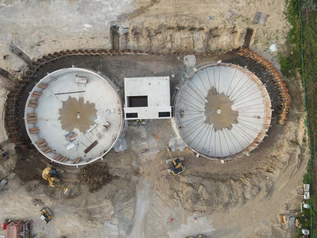 Aerial view of two large circular concrete tanks under construction.