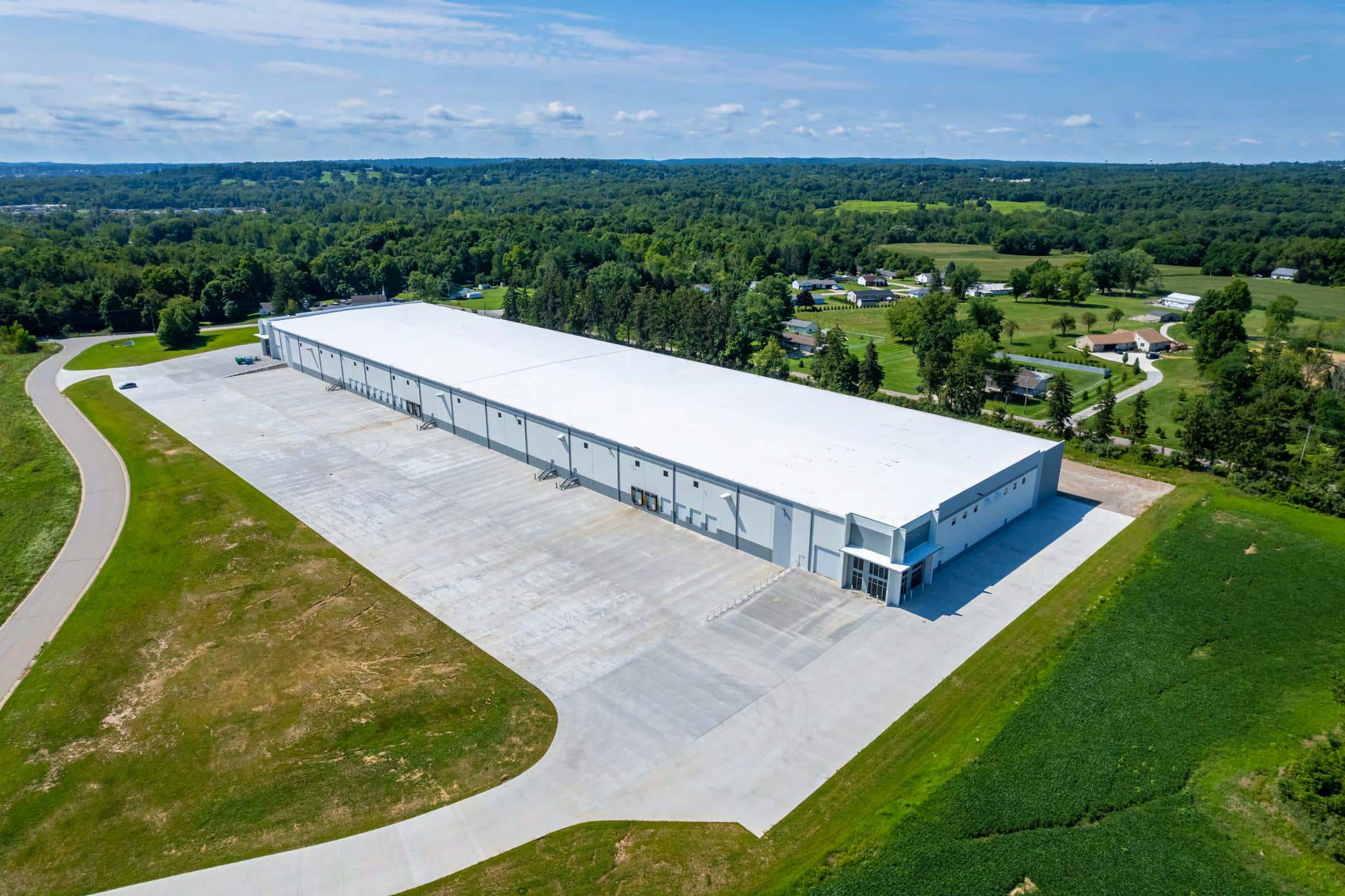 “Aerial view of a large, newly built industrial warehouse with a wide concrete apron, surrounded by green fields and rural landscape.