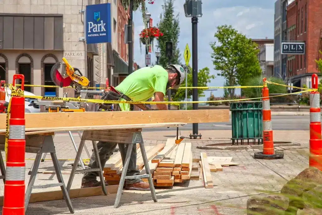 Man cutting wood in marked off area on sidewalk