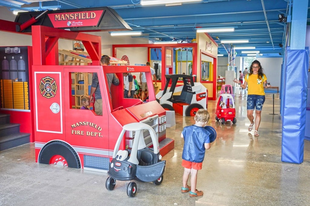 Children and caregivers at exhibit with large sculptural fire truck, building under construction, and other exhibits