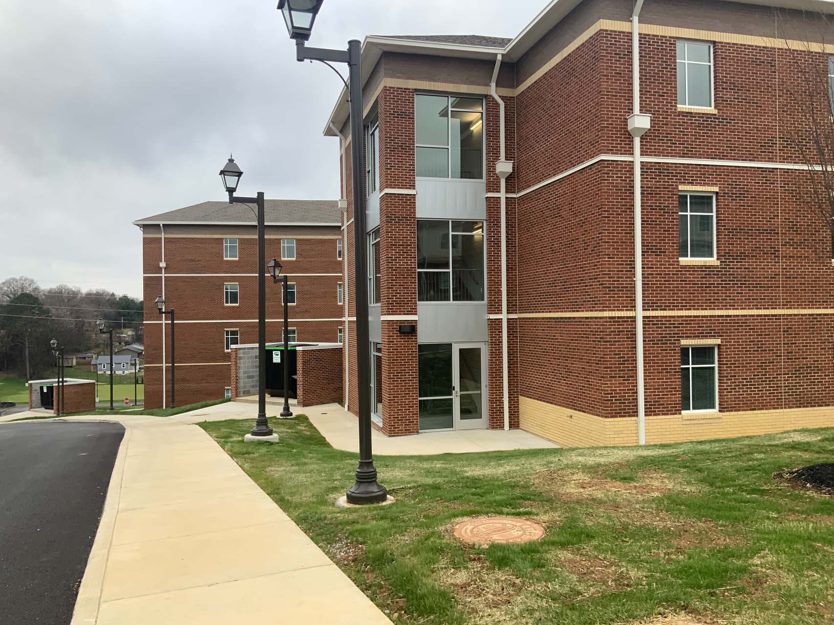 Three-story brick building with exterior walkways and a sidewalk in the foreground.
