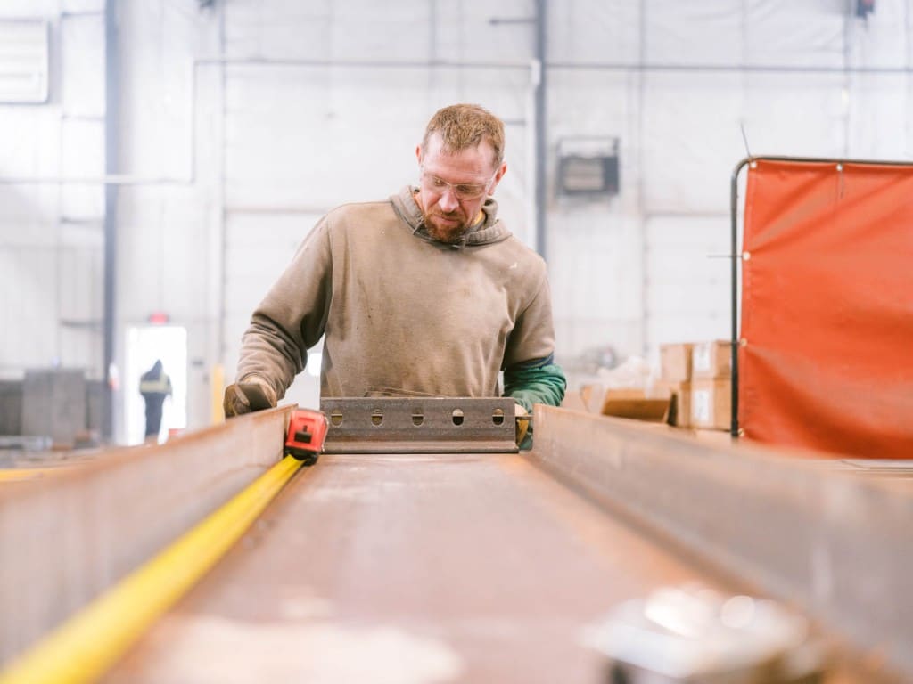 Worker measuring a steel beam in a fabrication shop.