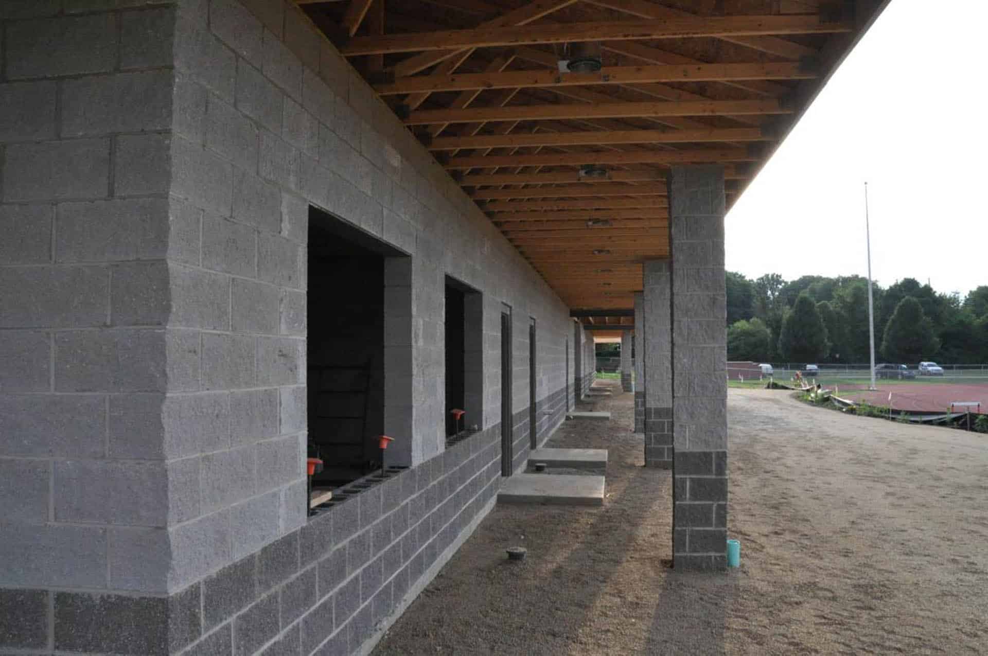 Exterior walkway of a partially constructed building with concrete block walls, open window openings, and exposed wooden roof framing.