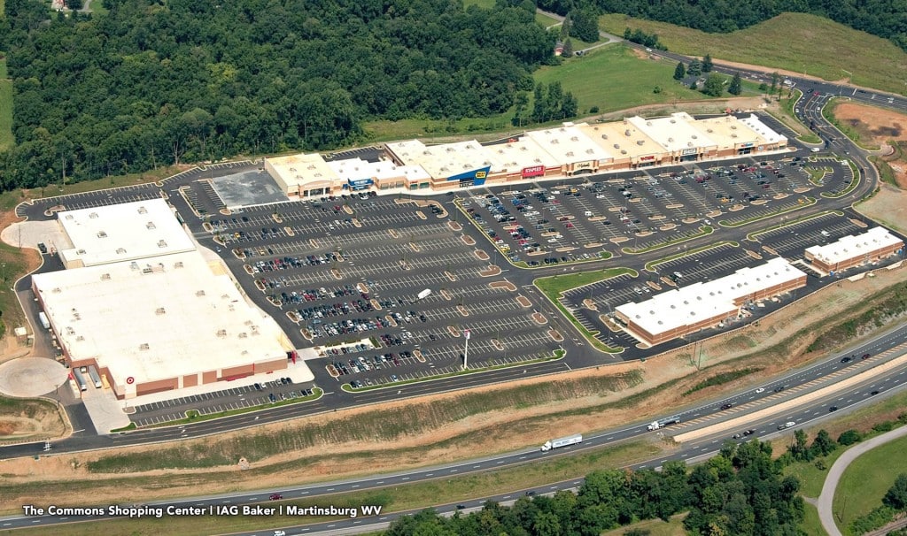 Aerial view of a large shopping center with multiple big-box stores and extensive parking lots, bordered by highways and surrounding greenery.