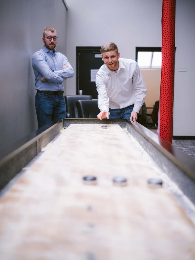 Two colleagues playing shuffleboard in an office break area.